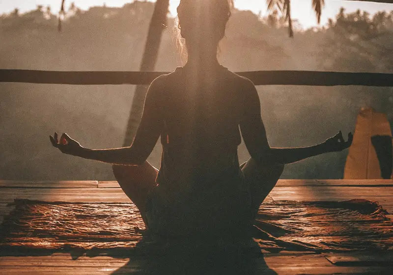 Person sitting cross-legged meditating at sunrise